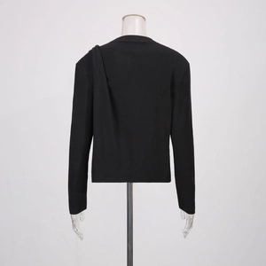 Détail d'un haut noir à manches longues avec drapé asymétrique sur l'épaule