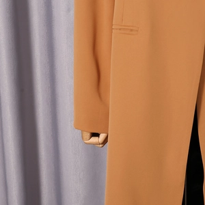 Detail view of camel long blazer showing smooth fabric texture and pocket flap design
