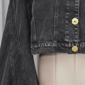 Detail of cropped washed black denim jacket featuring a unique gold eye-design button