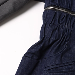 Détail macro d'une veste en jean montrant la fermeture éclair et le patchwork de cuir