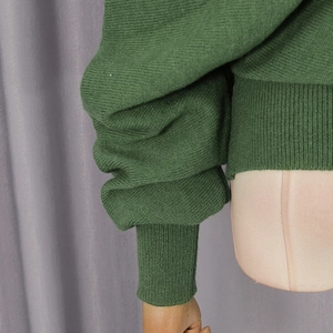 Close-up of deep green knit sweater featuring long ribbed cuffs and detailed side seams