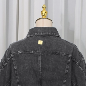 Detail of washed charcoal denim jacket featuring gold metal back logo plate and stitching