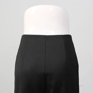 Detail view of high-waisted black trousers featuring elegant waist pleats and matte fabric