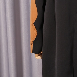 Detail of color-block blazer sleeve with decorative buttons and wavy contrast stitching