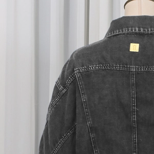 Detail of dark gray washed denim jacket featuring reinforced seams and golden square brand tag