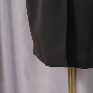 Detailed close-up showing the precise stitching and split hem of the black blazer jacket