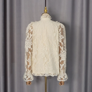Détail de la broderie en dentelle blanc crème et du col montant à volants sur le chemisier