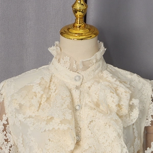 Détail du chemisier en dentelle à col montant volanté avec boutons perlés
