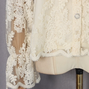 Détails de broderie en dentelle florale et boutons perles sur un chemisier beige