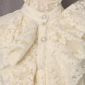 Détail du col en dentelle vintage avec boutons en perles et strass sur chemise écru