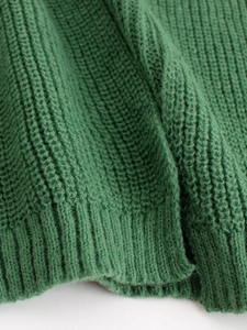 Close-up of dark green knitted cardigan showing thick texture and ribbed hem detail
