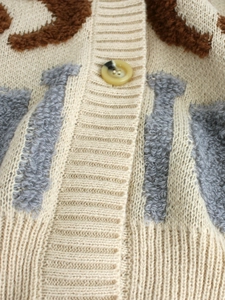 Gros plan du tissu d'un cardigan avec motif jacquard et détail d'un bouton en résine ambre