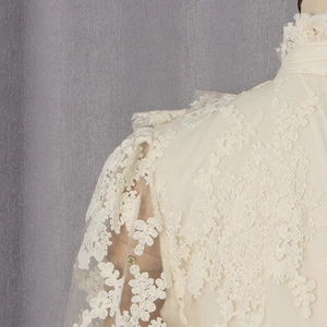Détail d'un haut en dentelle crème avec broderie florale 3D et manches bouffantes