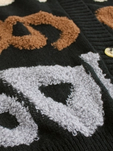 Détail macro d'un cardigan en maille avec motifs jacquard texturés et bouton ambré chic