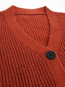 Close-up of rust red chunky knit cardigan featuring V-neck design and black button detail