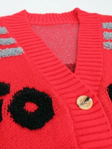 Détail du cardigan rouge en maille avec col en V, bord côtelé et bouton marbré