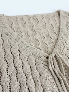 Gilet en maille ajourée beige avec col en V et texture bohème sur un fond blanc épuré
