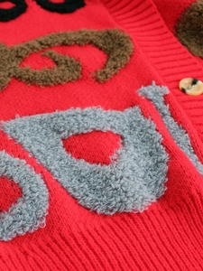 Détail d'un cardigan rouge avec broderie lettre texturée et bouton ambré élégant