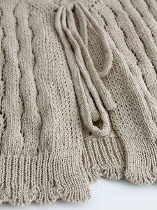 Gros plan détaillé d'un cardigan beige en maille torsadée avec ourlet côtelé et cordon assorti