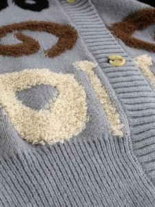 Détail du cardigan gris montrant la broderie de lettres bouclées et la maille côtelée du col