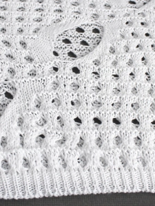Vue macro du tricot crochet blanc montrant la maille ajourée et l'ourlet à bords côtes