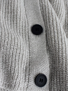 Detailed macro view of light gray chunky knit cardigan texture and black matte buttons