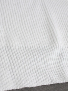 Close-up of white rib-knit fabric texture showing elastic weave on a long sleeve sweater