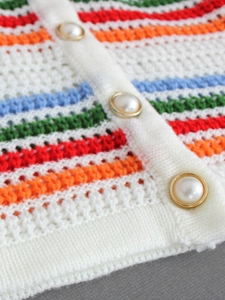 Macro detail of knit cardigan showing colorful stripes and ornate pearl buttons