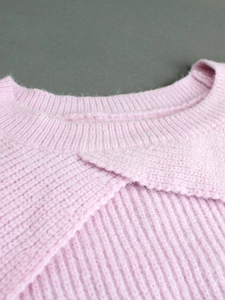 Detail of light pink knit sweater featuring a ribbed crew neck and layered front design