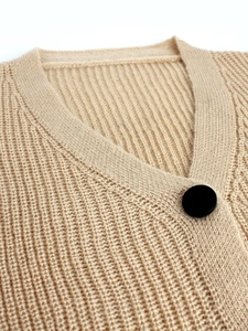 Close-up of beige knit cardigan featuring a V-neckline and large black button detail
