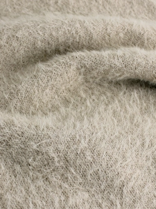 Close-up of soft beige knit fabric showing high-quality fuzzy plush texture and fibers