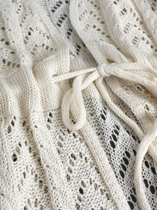 Detail of cream crochet knit fabric with intricate geometric patterns and drawstring cord