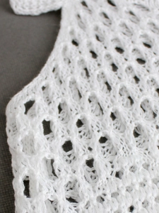 Close-up of white knit tank top with hollow diamond crochet pattern and mesh texture