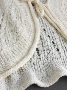 Detail of white crochet knit cardigan featuring intricate hollow patterns and tie-up drawstring