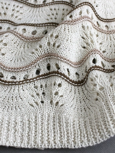 Détail d'un motif en tricot ondulé ajouré avec rayures marron sur un pull en maille beige