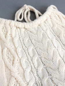 Dettaglio di un top smanicato in maglia intrecciata color crema con lacci decorativi