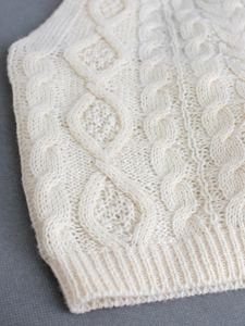 Dettaglio macro della maglia a trecce crema e dell'orlo a costine di un gilet