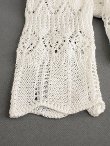 Gros plan sur les motifs de dentelle ajourée d'un gilet en maille fine blanc pour femme