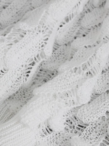 Close-up of white hollow-out knit fabric showing intricate lace patterns and ribbed hem
