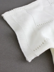 Detailed view of white knit top showing intricate hollow pointelle and wavy scalloped edge