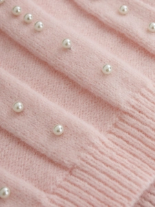 Macro shot of pink knit sweater featuring white pearl embellishments and ribbed texture