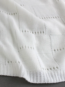 Macro view of white pointelle checkered knit fabric with ribbed edge detail