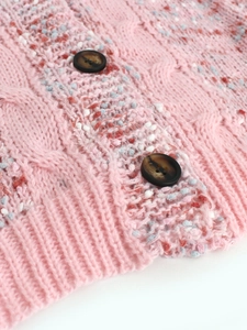 Detail of pink knit cardigan showing cable stitch patterns and brown buttons