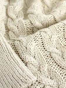 Dettaglio del maglione in maglia avorio che mostra la spessa trama a trecce e il tessuto morbido