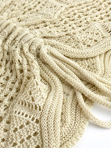 Detail of beige crochet knit beach cover-up with intricate hollow patterns and drawstring