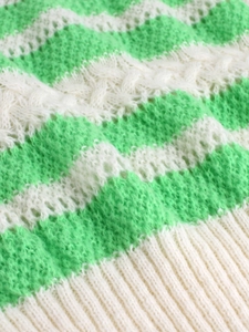 Detailed close-up of green and white striped knit sweater with wavy hollow textures