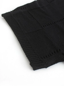 Close-up of black knit sweater with checkerboard texture and delicate hollow-out details