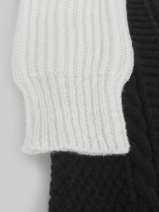 Detailed macro view of the white ribbed knit cuff and black textured knit sweater fabric
