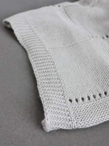 Detailed view of light grey knit fabric featuring pointelle patterns and ribbed edges