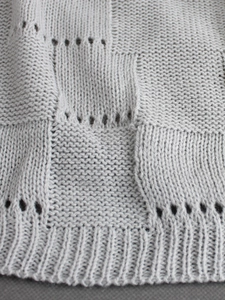 Detailed macro view of light gray knit fabric with hollow patterns and ribbed cuffs